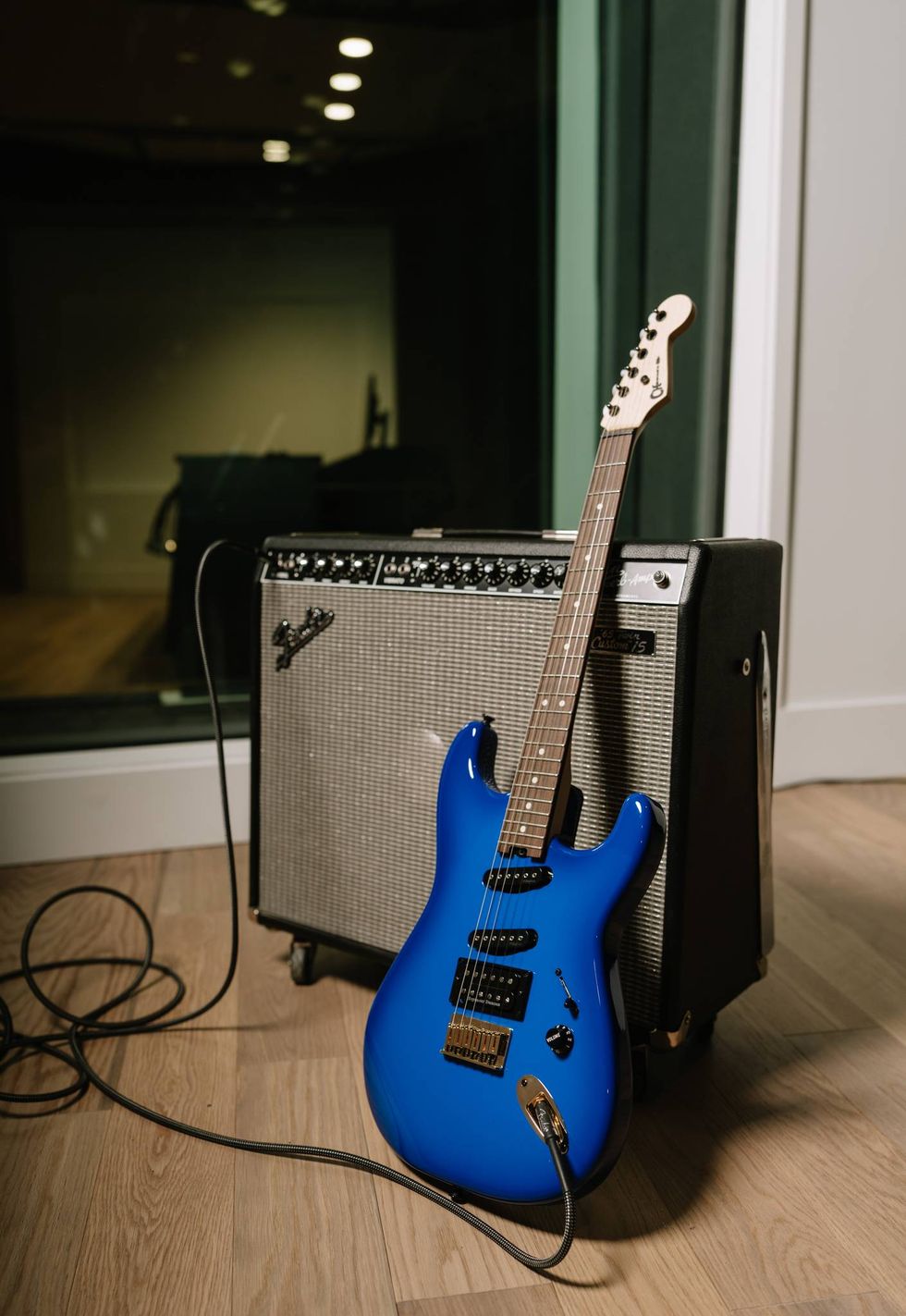 A blue electric guitar propped against a vintage amplifier on wooden flooring.