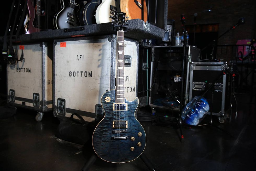 A blue electric guitar stands in front of music equipment cases at a concert venue.
