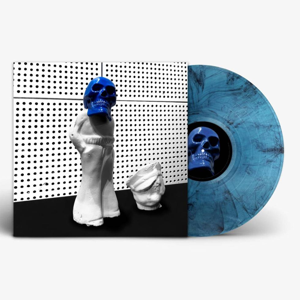 A blue skull figurine stands on a black backdrop next to a marbled blue vinyl record.