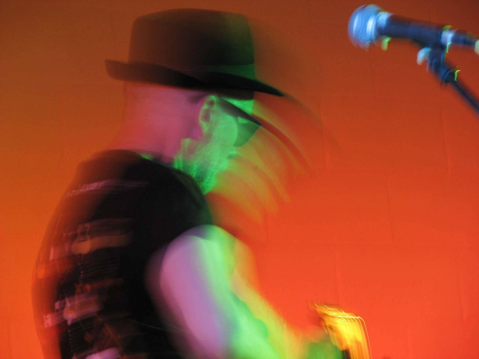 A blurred figure of a musician in a hat, illuminated by colorful stage lights.