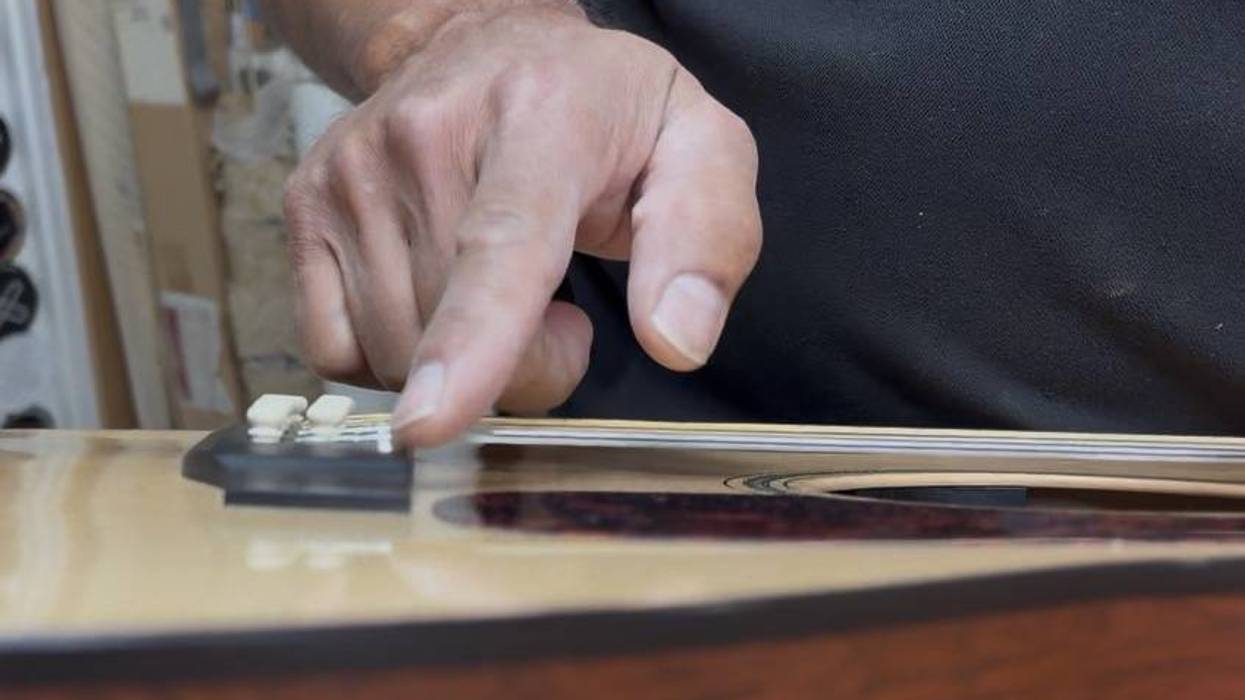 A close-up of a hand pressing a string on an acoustic guitar's bridge.
