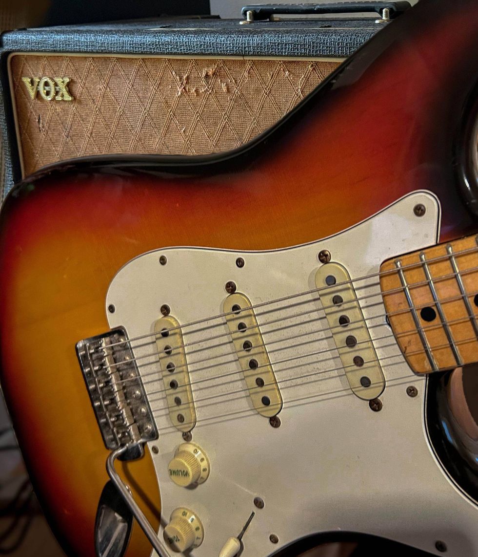 A close-up of a sunburst electric guitar next to a vintage Vox amplifier.