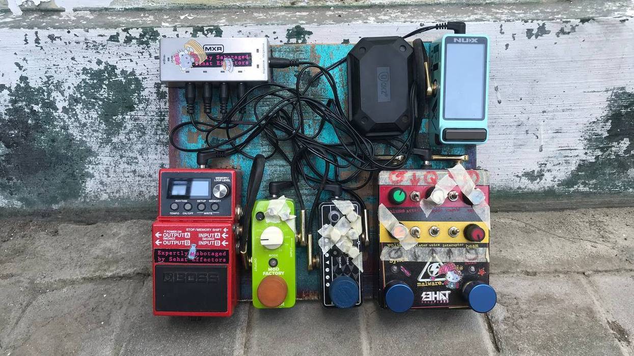 A collection of assorted guitar pedals arranged on a worn wooden board.
