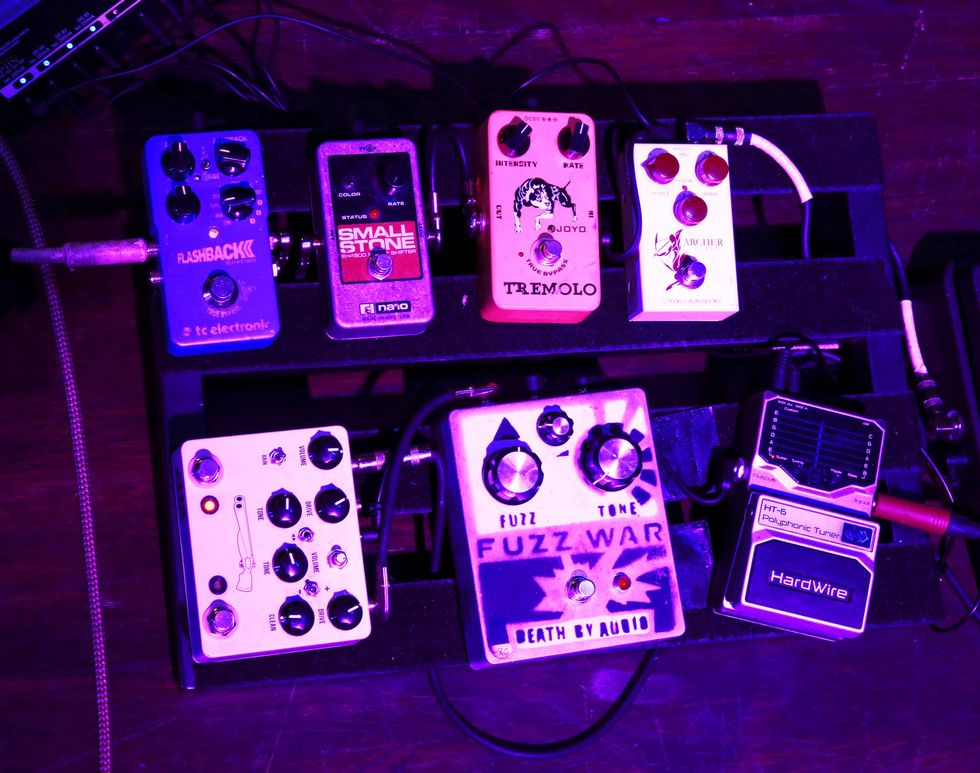 A collection of guitar pedals on a pedalboard with vibrant purple lighting.