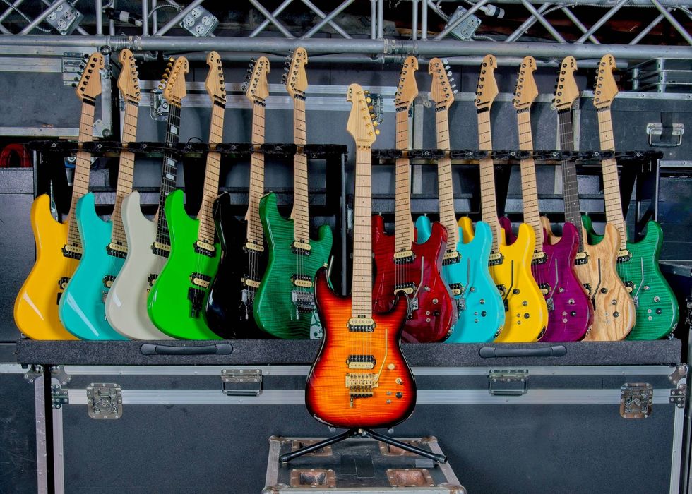 A colorful array of electric guitars displayed on stands against a backdrop.