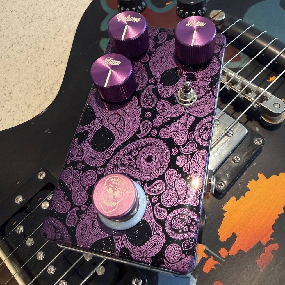 A colorful guitar pedal with purple knobs and intricate paisley designs, sitting on a guitar.