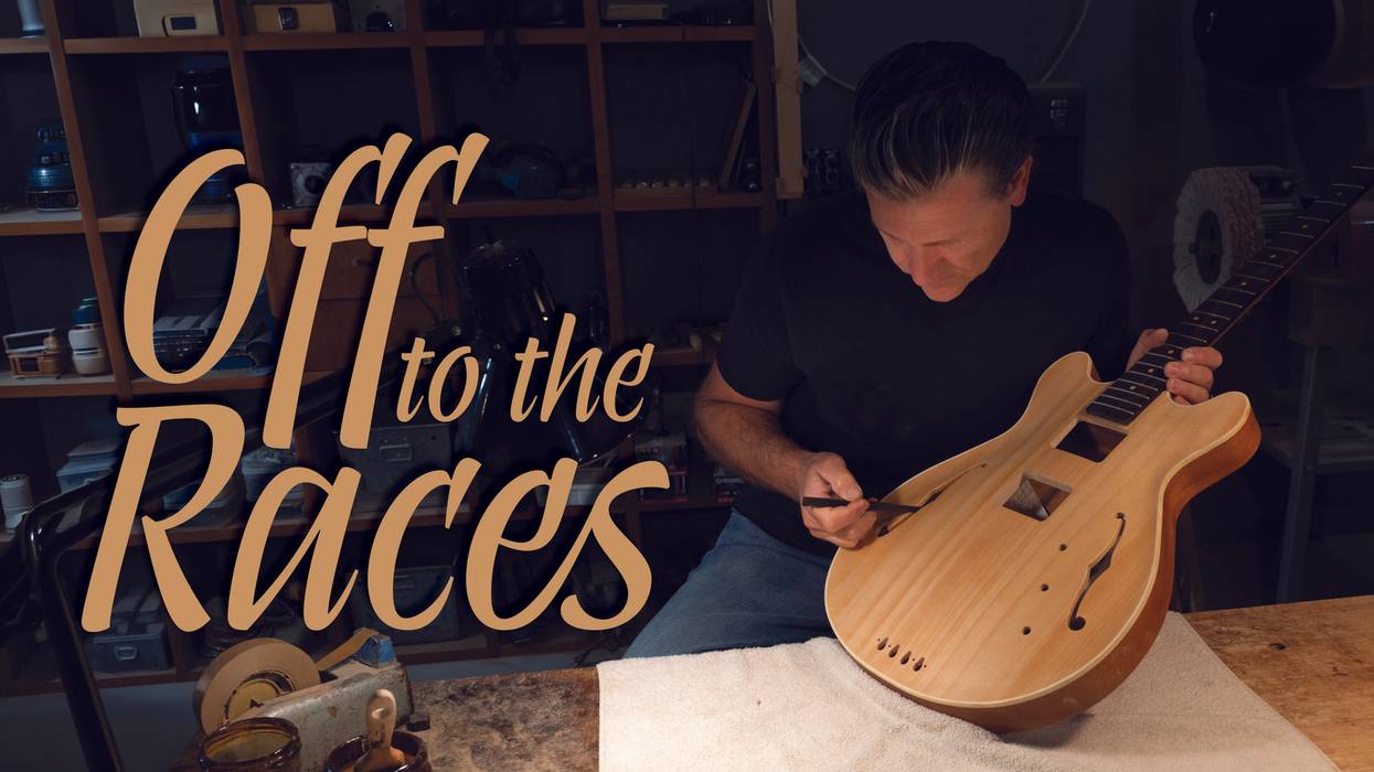 A craftsman meticulously works on an unfinished guitar in a workshop.