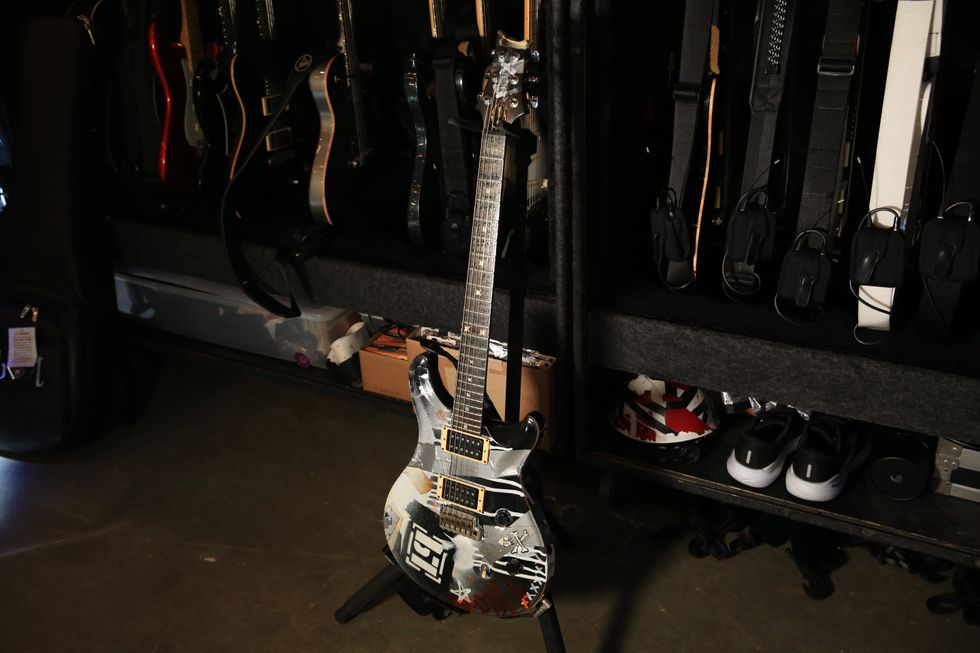 A custom-painted electric guitar stands on a floor amid various other guitars and gear.