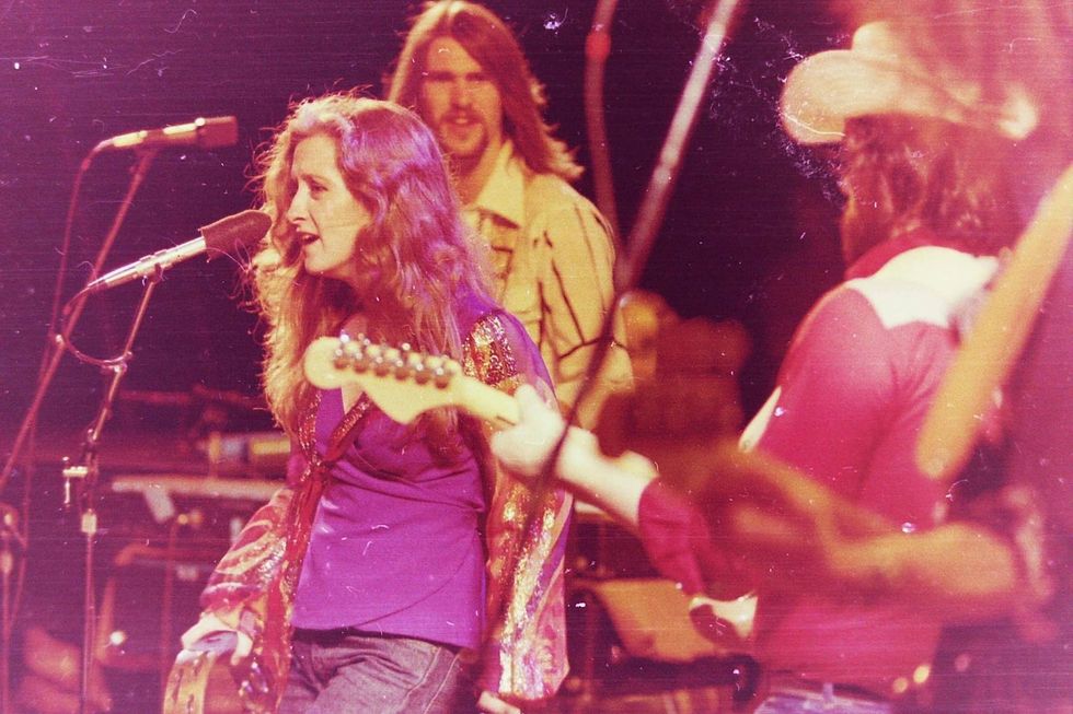 A female singer performs on stage, with musicians visible in the background.