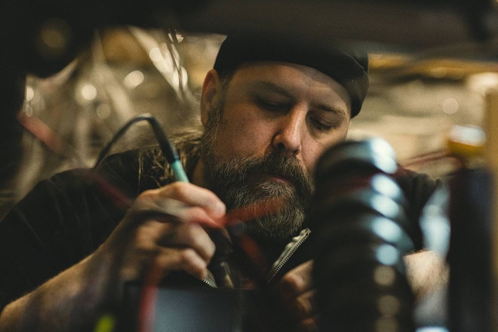 A focused technician works on electronic wiring in a dimly lit workshop.