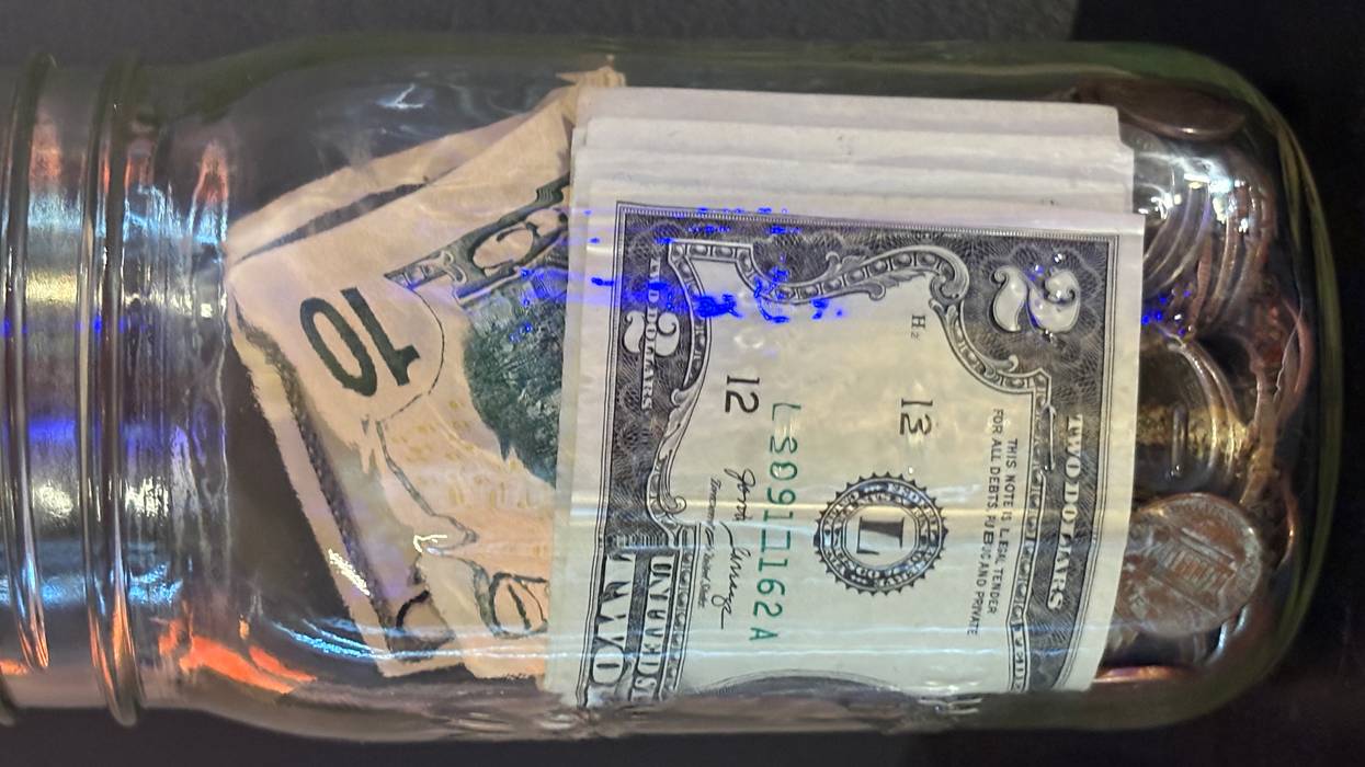 A glass jar filled with bills and coins, including a folded $10 and $2 note.