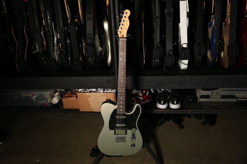 A green electric guitar stands in front of a rack filled with various guitars.