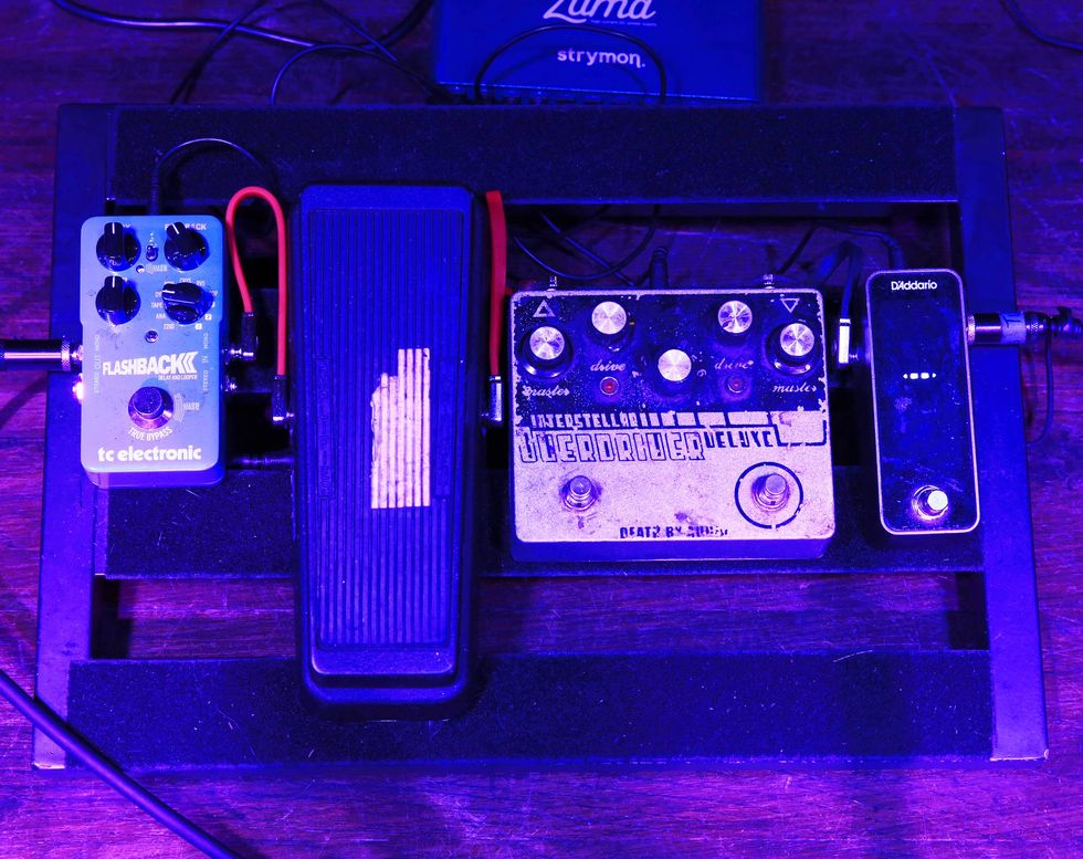 A guitar pedalboard displaying various effects pedals and a volume pedal, illuminated softly.