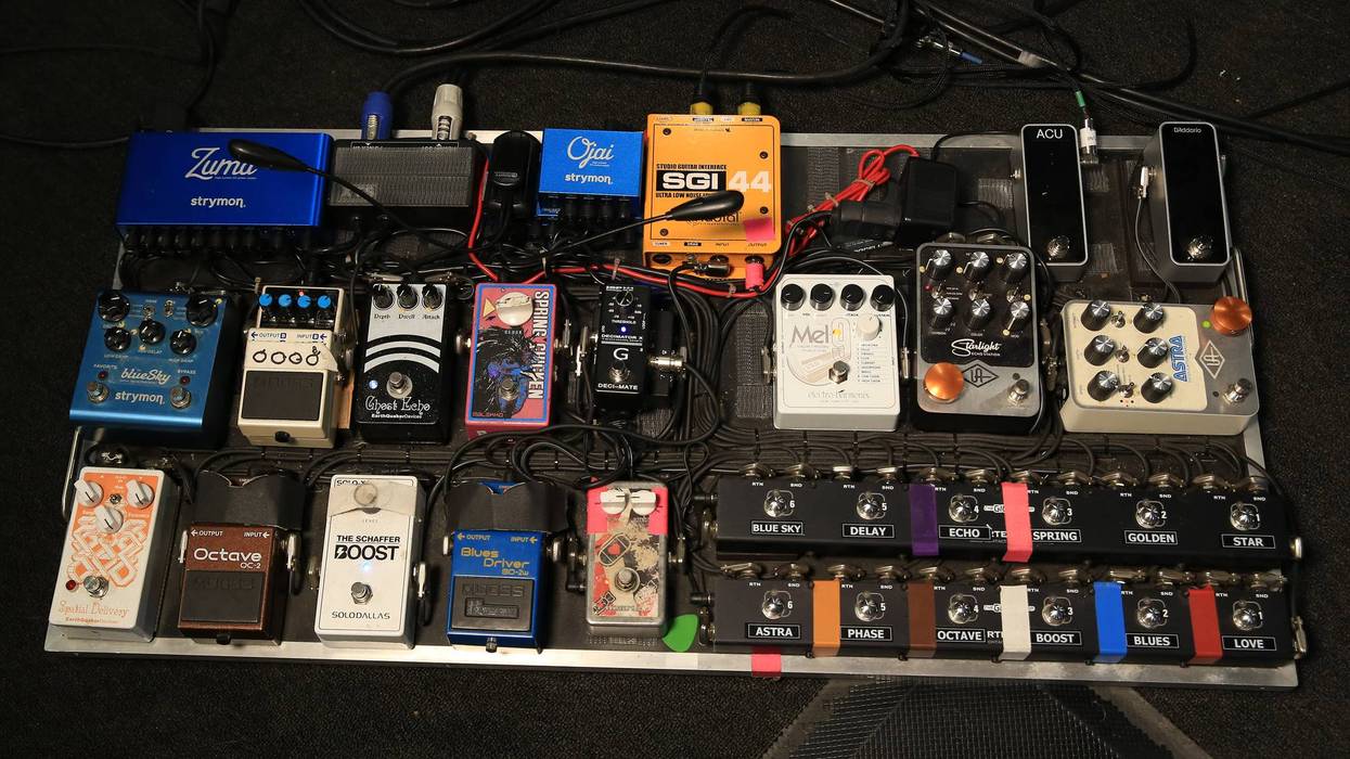 A guitar pedalboard featuring various effects pedals, cables, and power supplies arranged neatly.