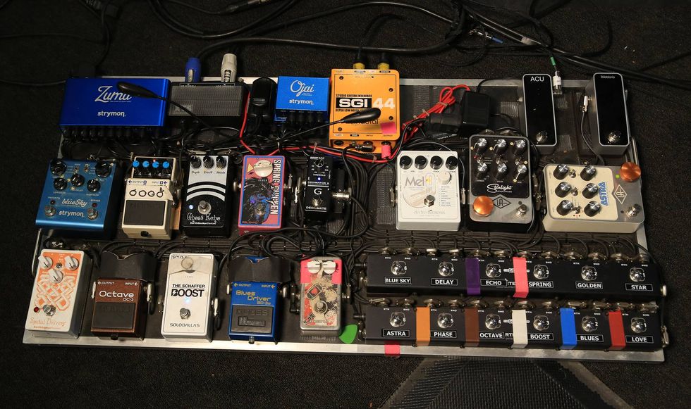 A guitar pedalboard featuring various effects pedals, cables, and power supplies arranged neatly.