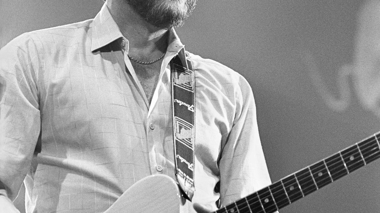 A guitarist smiles and plays on stage under bright lights.