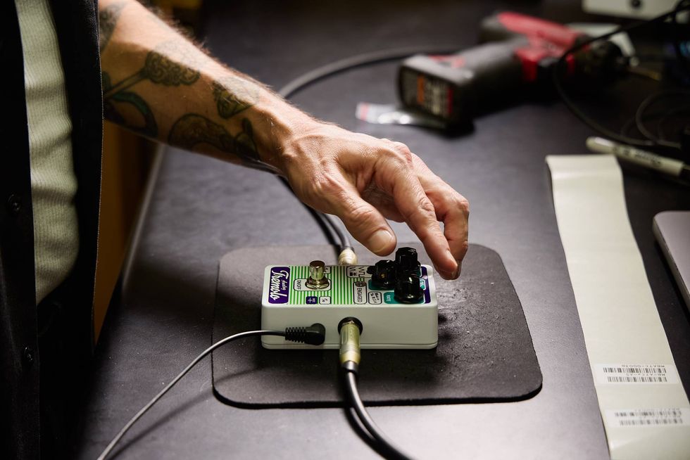 A hand adjusts knobs on a white guitar effects pedal on a workbench.