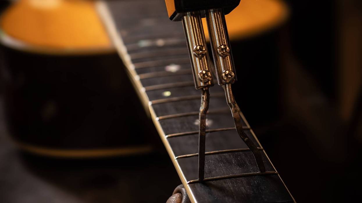 A hand using a tool on a guitar fretboard, with a blurred guitar body in the background.
