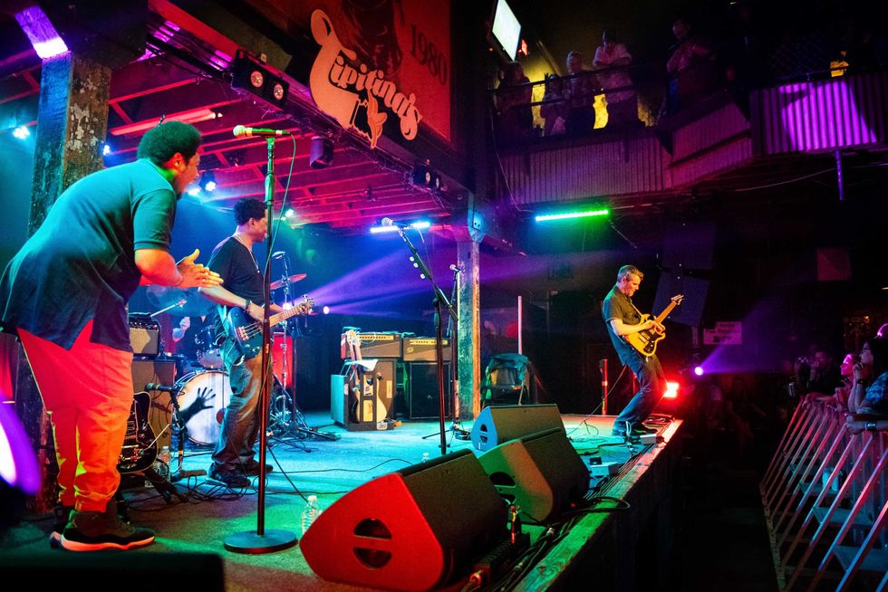 A live band performs on stage with colorful lights, energetic crowd, and instruments.