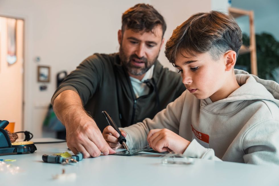 A man guides a boy in a crafting project at a table, focusing on their task.