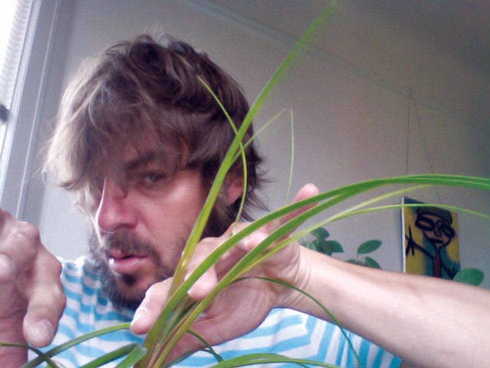 A man with messy hair carefully examines a green plant, sitting indoors.
