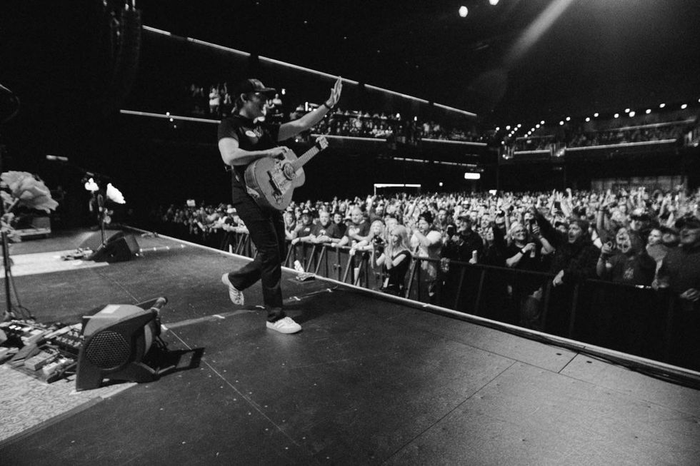 A musician on stage plays guitar, engaging a cheering crowd in a lively performance.