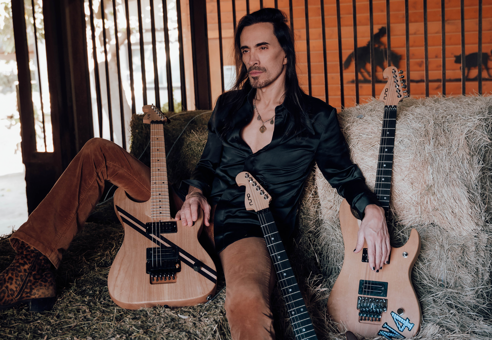 A musician sits on hay, surrounded by electric guitars, exuding a stylish rock vibe.