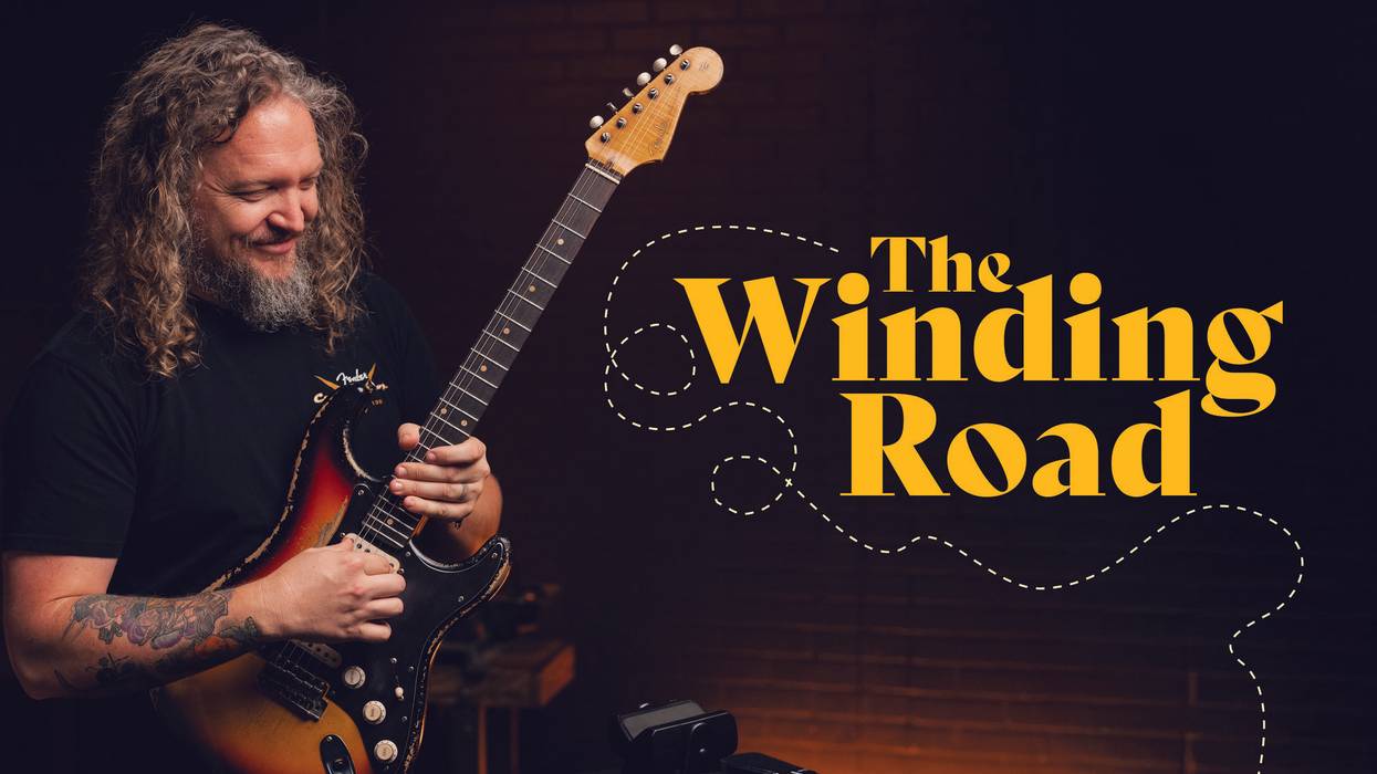 A musician with curly hair smiles while playing an electric guitar, titled "The Winding Road."