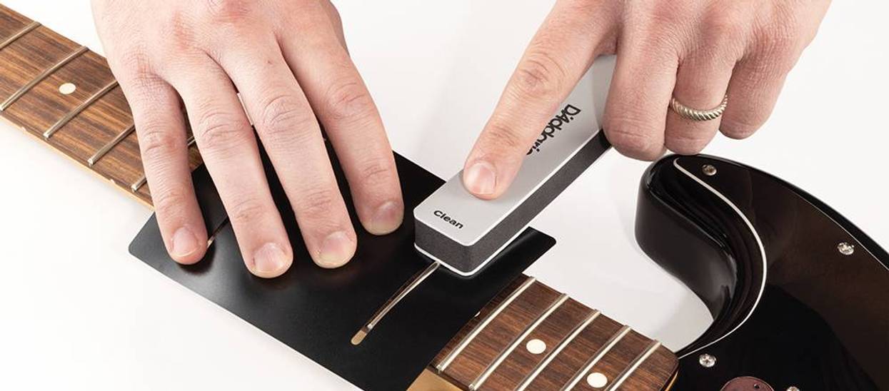 A person cleans a guitar fretboard with a specialized tool.
