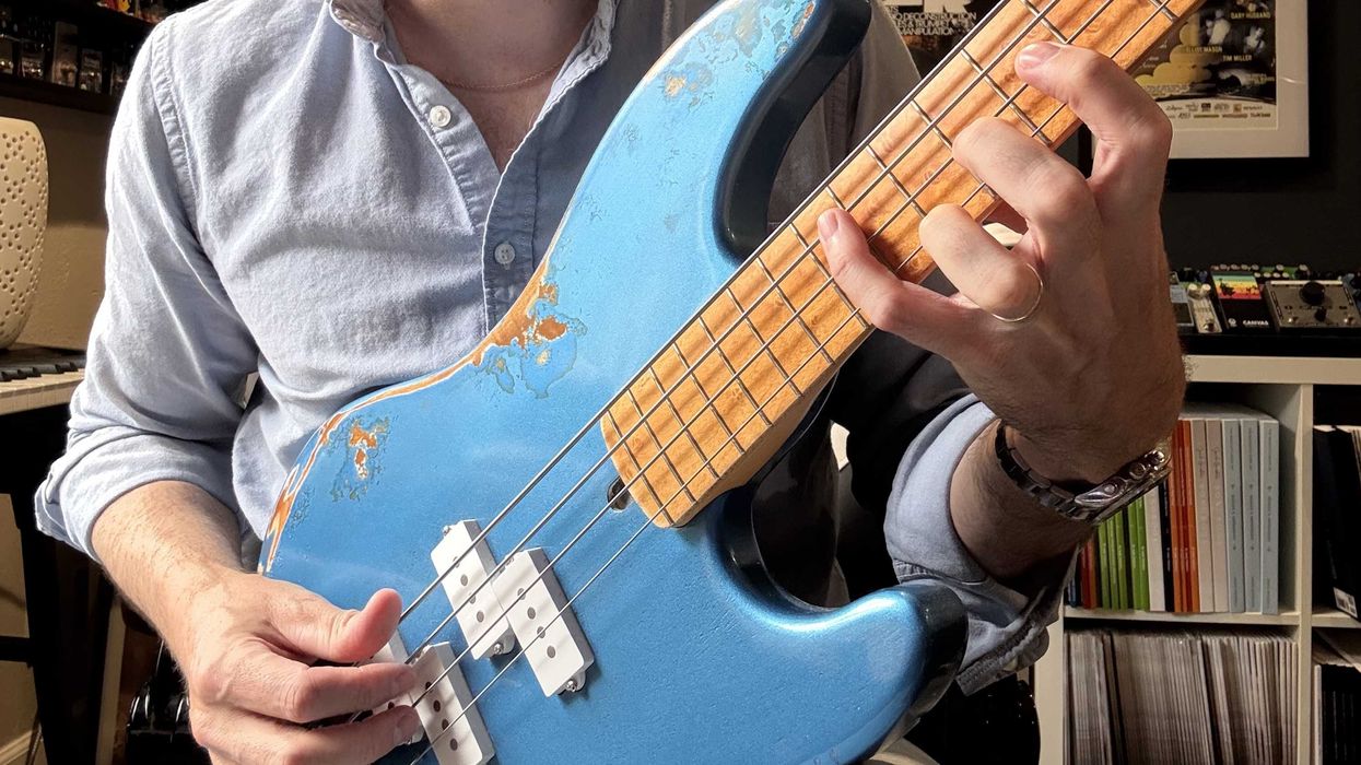 A person playing a blue bass guitar with a worn finish and wooden neck.