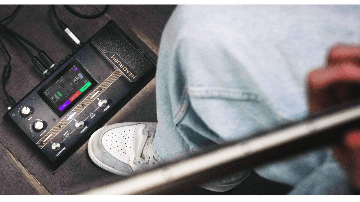 A person playing guitar next to a guitar effects pedal on the floor.