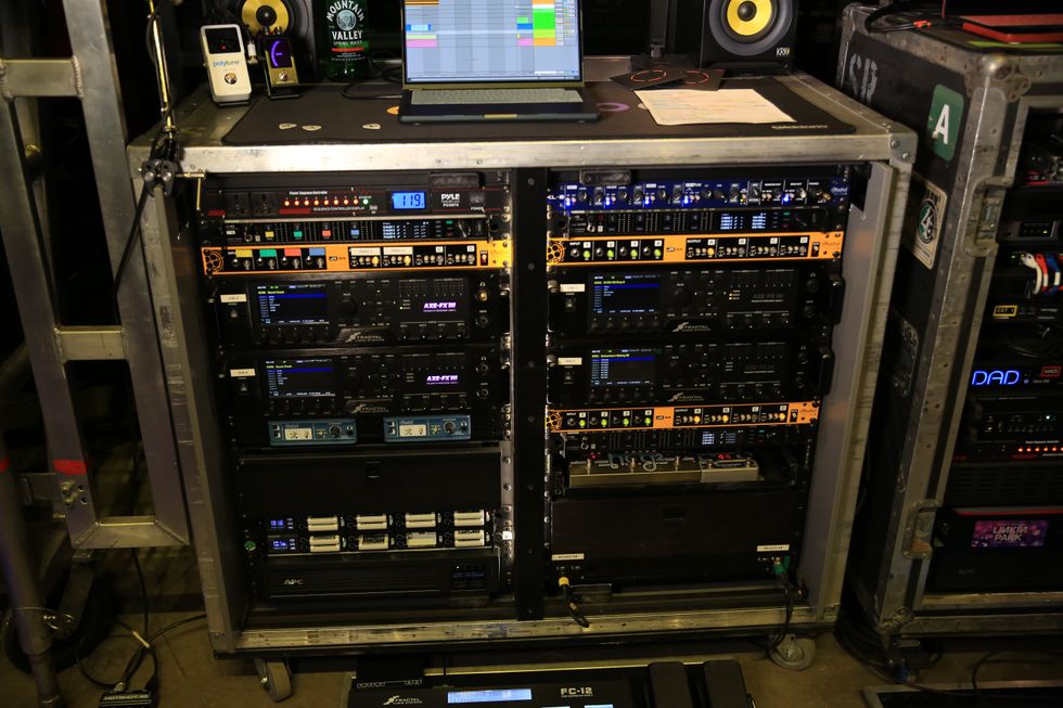 A rack of audio equipment with digital displays and a laptop on top, set up for a performance.