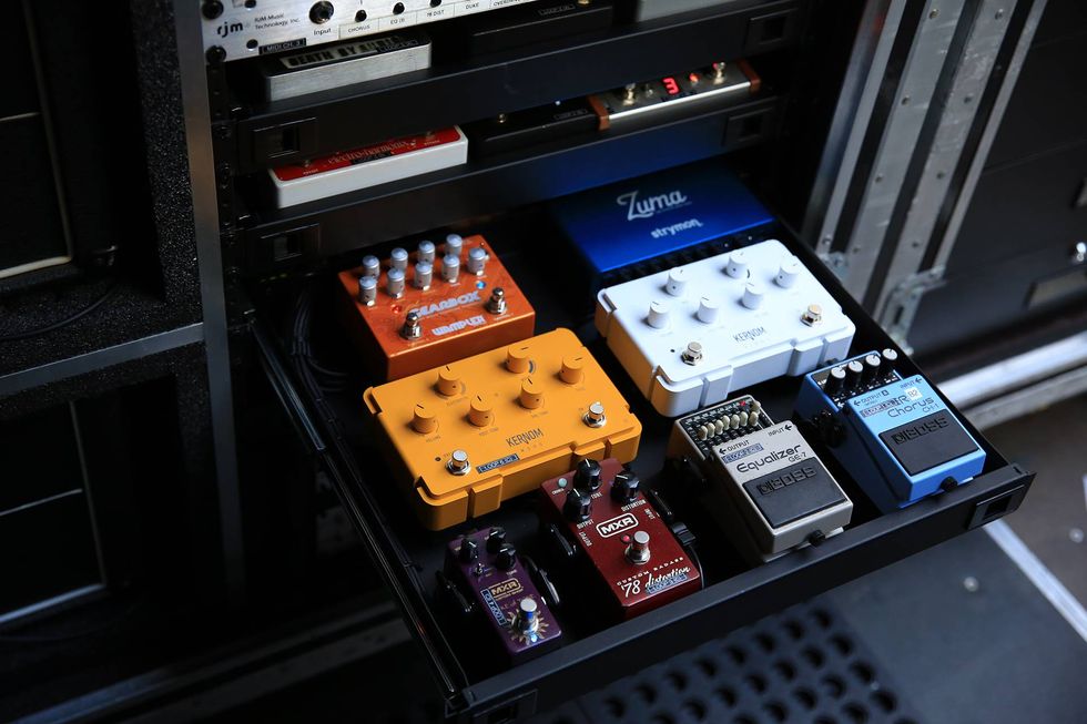 A rack of guitar effects pedals in various colors, organized on a drawer.