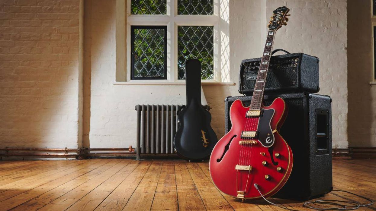 A red electric guitar rests on an amp, with a black case and window in a bright room.