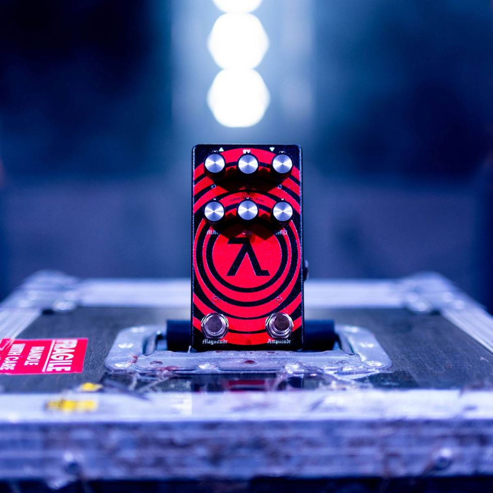 A red guitar pedal with knobs, resting on a flight case under soft lighting.