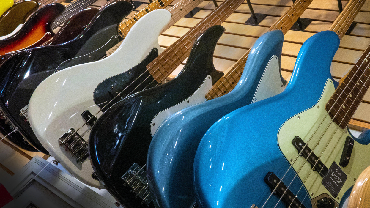 A row of colorful electric bass guitars displayed on a wooden rack.