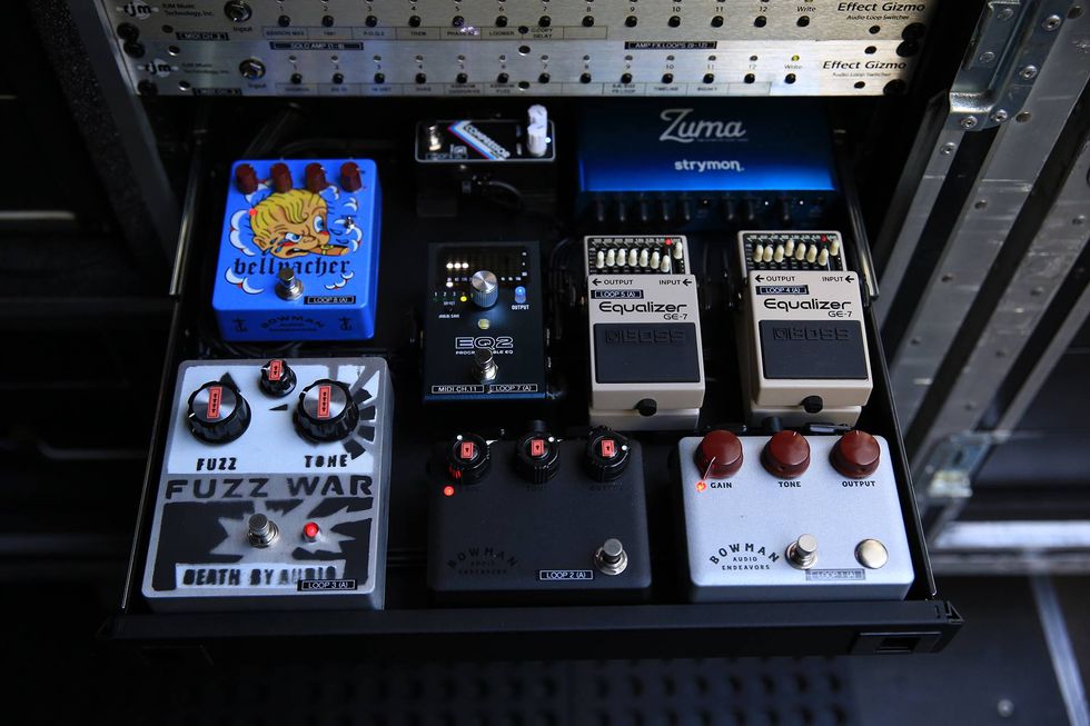 A row of various guitar effect pedals, including fuzz, equalizers, and a loop pedal.