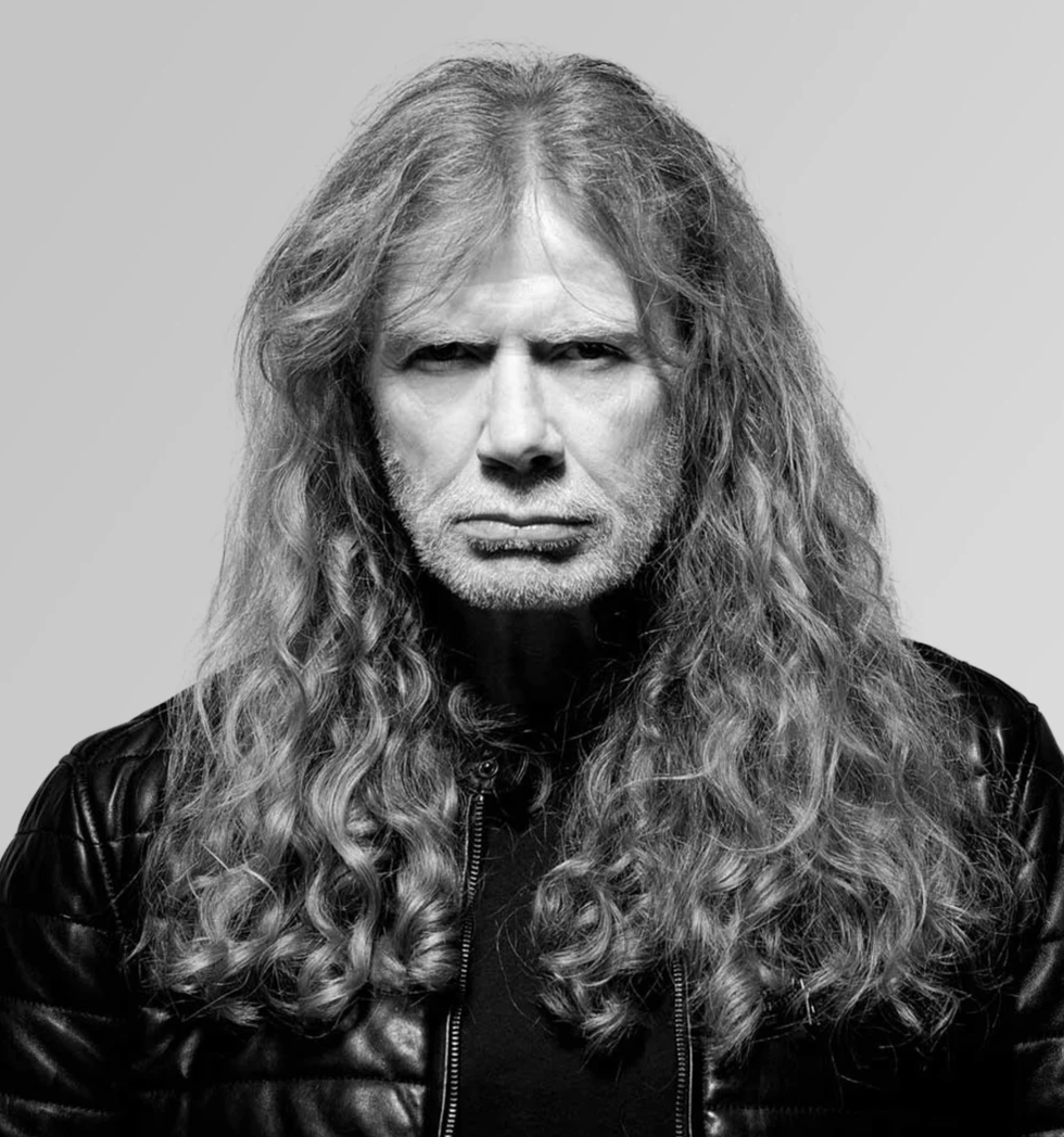 A serious-looking man with long, curly hair and a leather jacket against a gray background.
