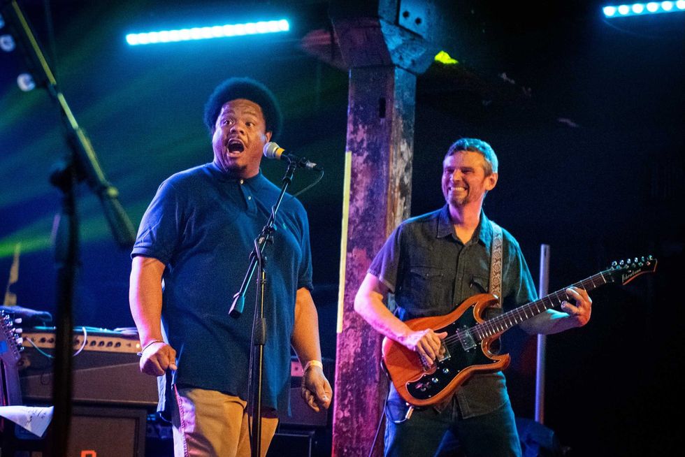 A singer and guitarist perform energetically on stage with colorful lights.