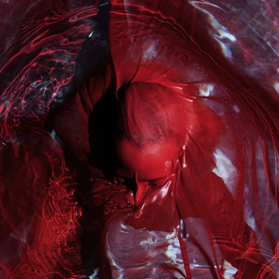 A submerged figure partially enveloped in flowing red fabric and water, creating a surreal effect.