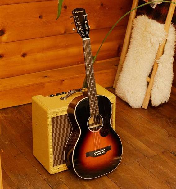 A sunburst acoustic guitar leans against a yellow amplifier on wooden floorboards.