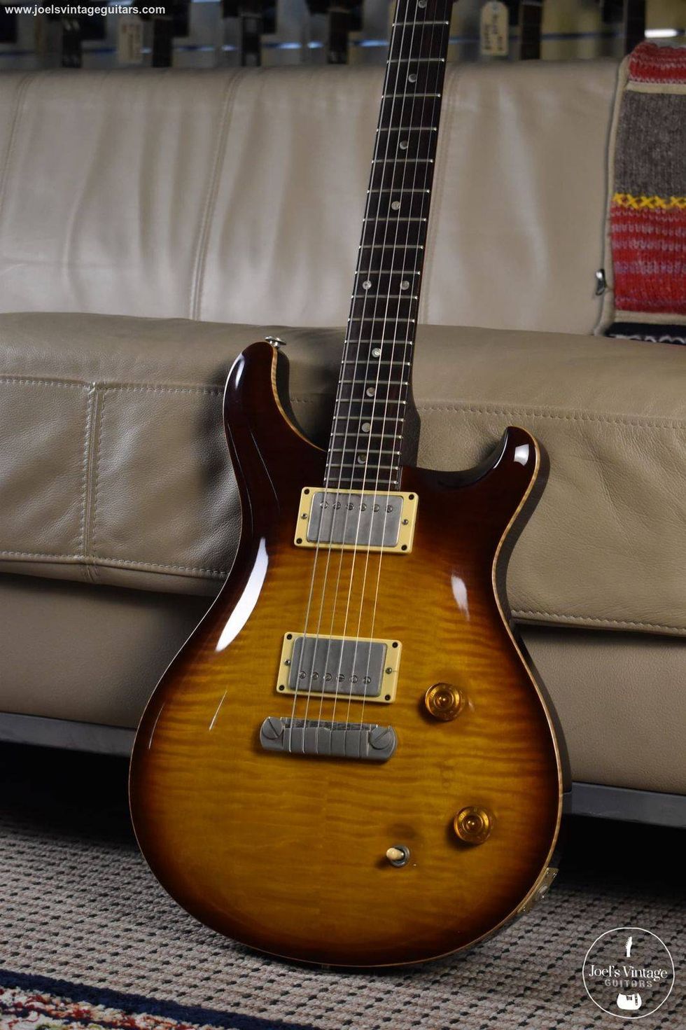 A sunburst electric guitar rests on a beige couch with a patterned rug beneath it.