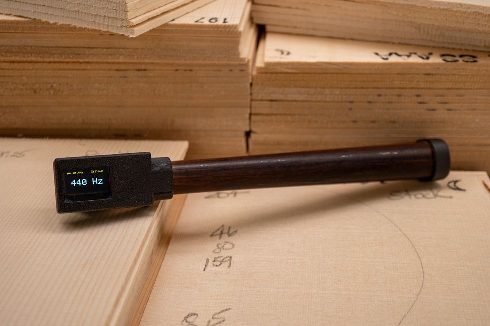A tuning fork displaying 440 Hz, resting on a stack of wooden boards with markings.