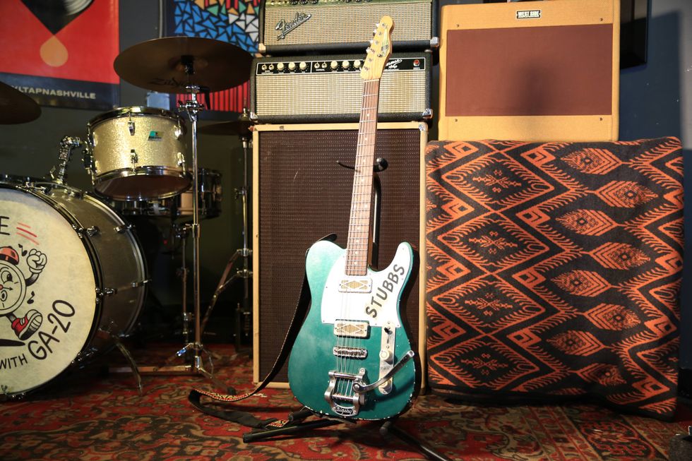 A turquoise guitar labeled "STUBBS" stands beside drums and amplifier stacks.
