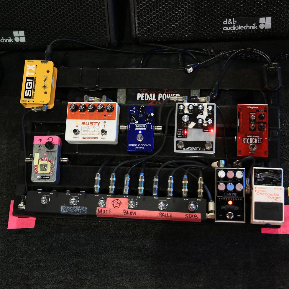 A variety of guitar pedals arranged on a pedalboard with labeled connections.