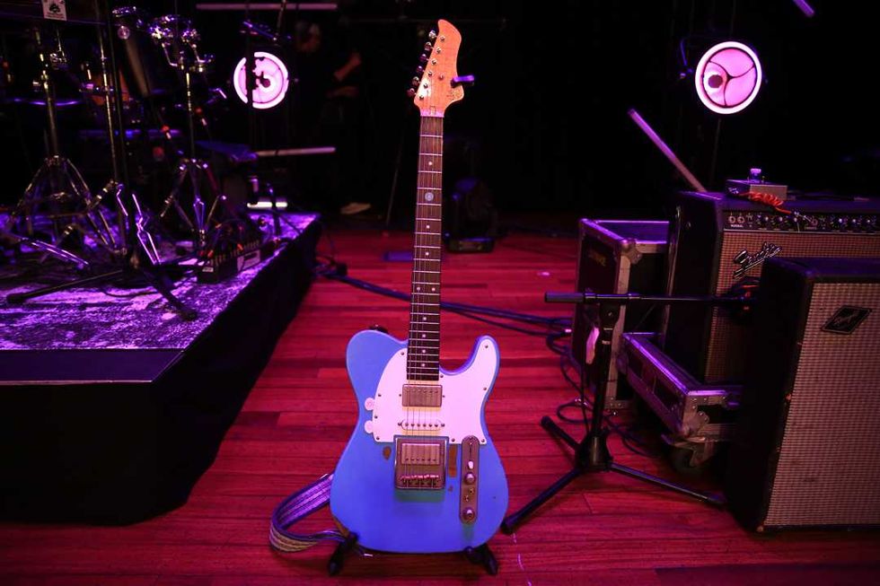 A vibrant blue electric guitar stands on stage, surrounded by music equipment.