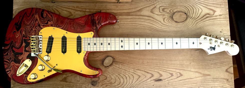 A vibrant red and black electric guitar with a yellow pickguard, resting on a wooden surface.