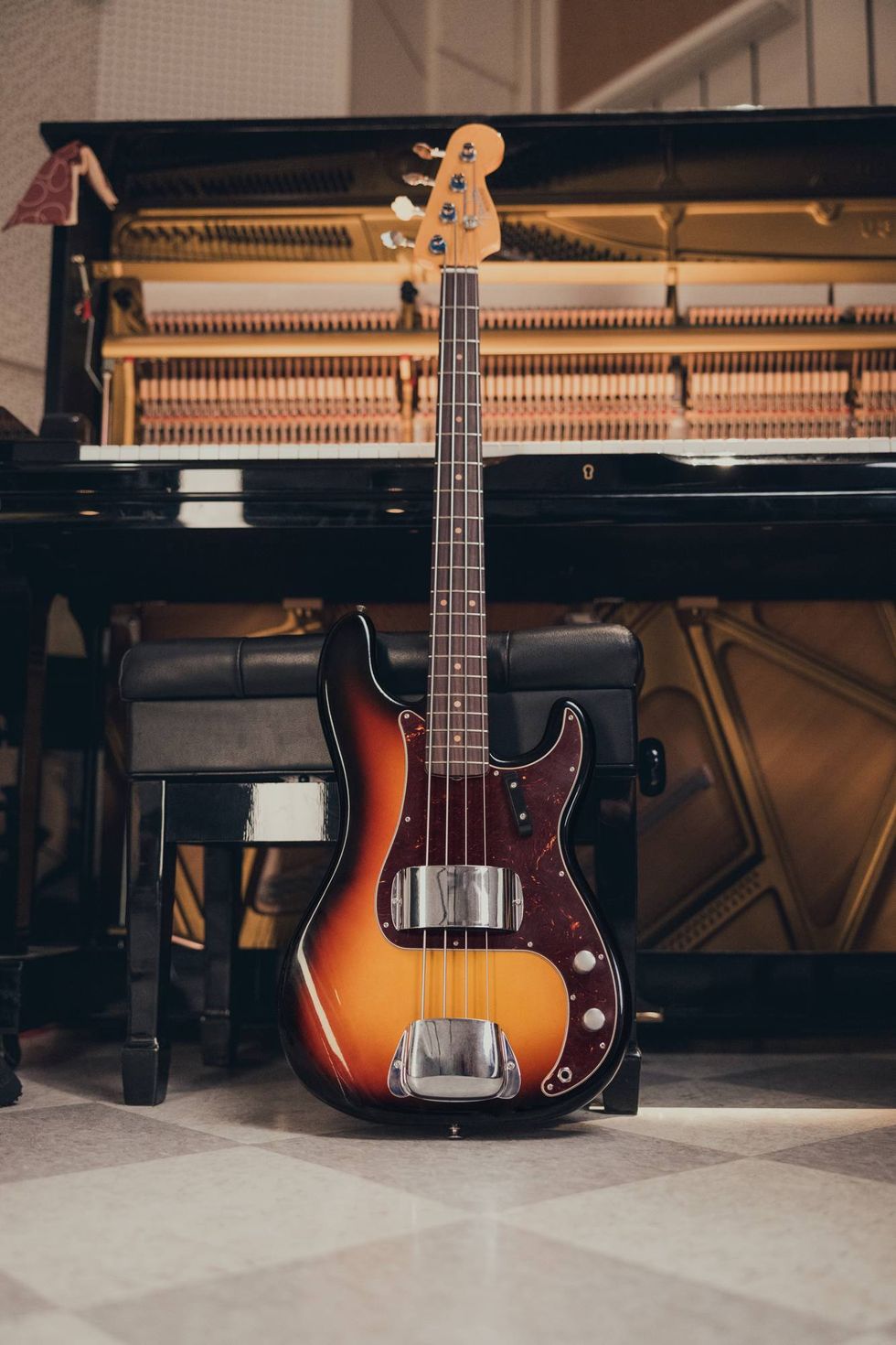 A vintage bass guitar stands beside a black piano on a checkered floor.