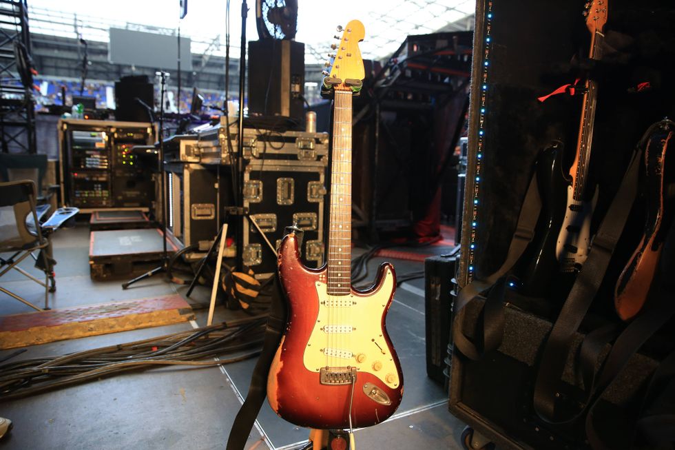 A vintage electric guitar stands on stage next to music equipment in a concert setting.