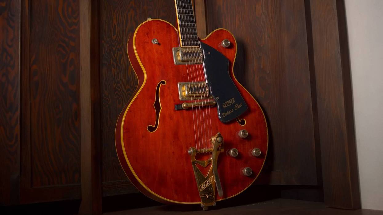 A vintage Gretsch guitar with a glossy orange finish, displayed against a wooden backdrop.